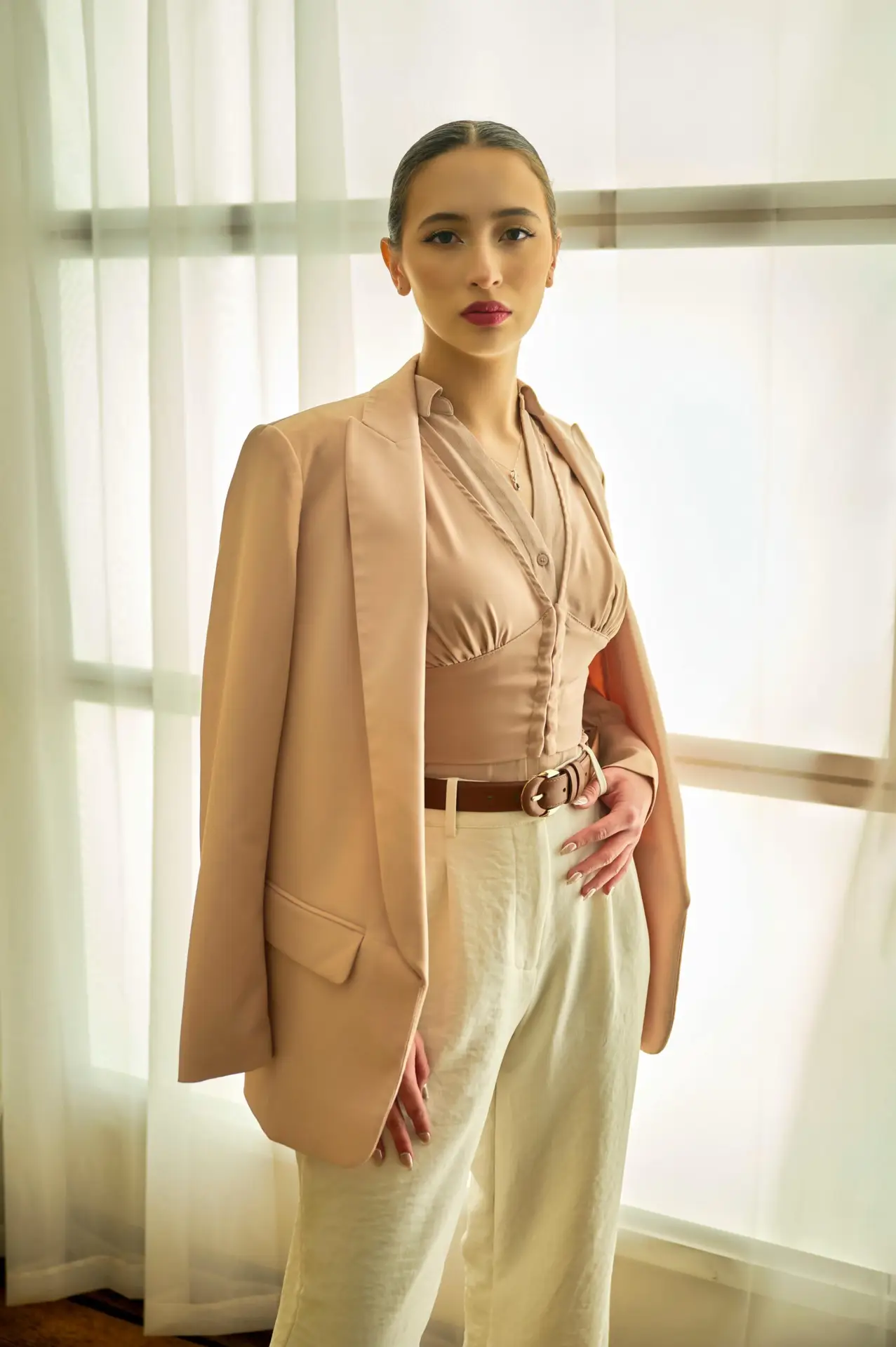 Young woman posing confidently in chic neutral clothing indoors with natural light.