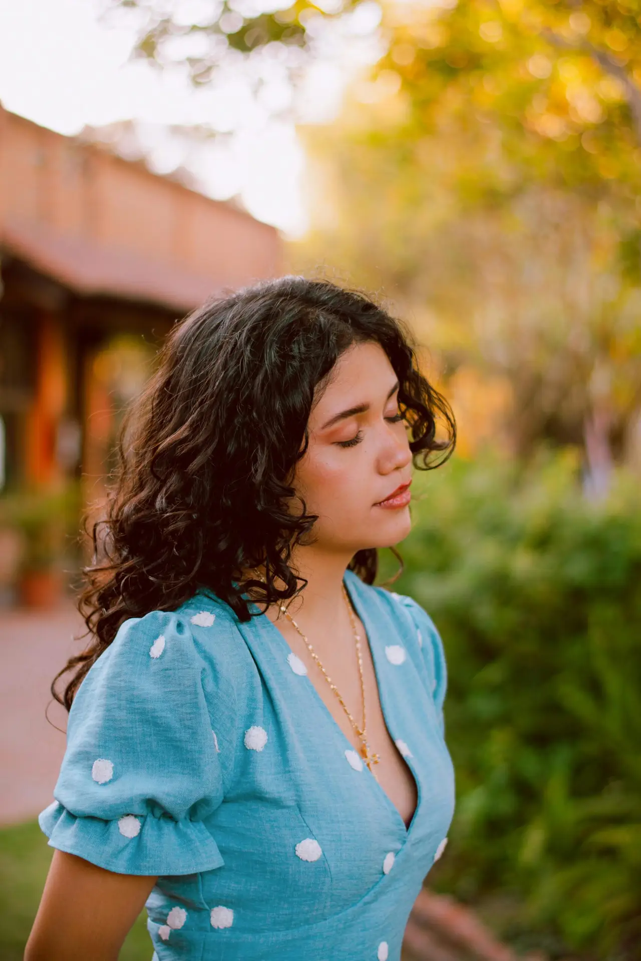 Peaceful woman in blue dress enjoying sunset outdoors in a garden setting.